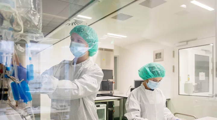 Zwei Forscherinnen stehen in einem Labor. Sie tragen Schutzkleidung, ein Haarnetz, Mundschutz und Handschuhe.