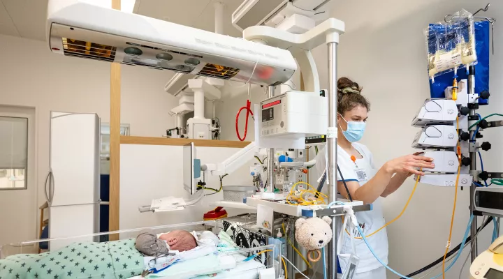 Pflegefachfrau Neonatologie macht Einstellungen am Infusionsständer nähe Spitalbett