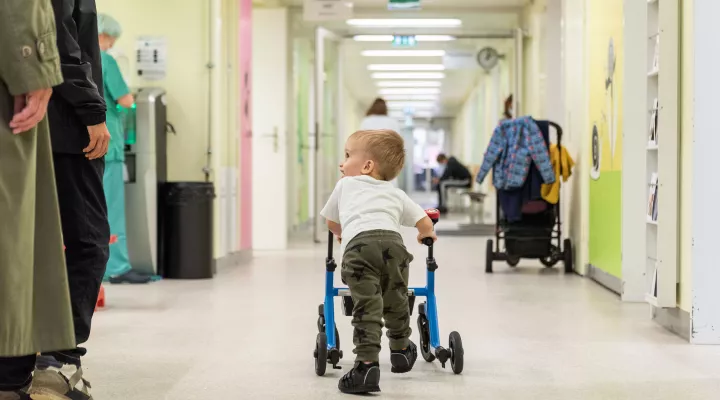 Ein Junge läuft mit seinem Rollator durch den gang des Kinderspitals während die Passanten ihn anschauen