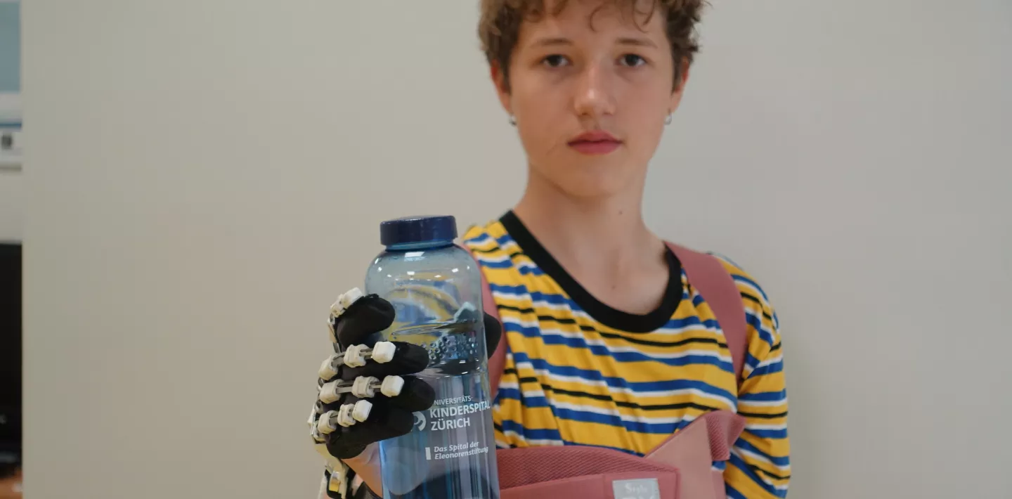 Junge hält mit PEXO Hand-Exoskelett eine Trinkflasche. 