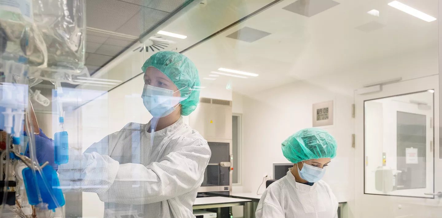 Zwei Forscherinnen stehen in einem Labor. Sie tragen Schutzkleidung, ein Haarnetz, Mundschutz und Handschuhe.