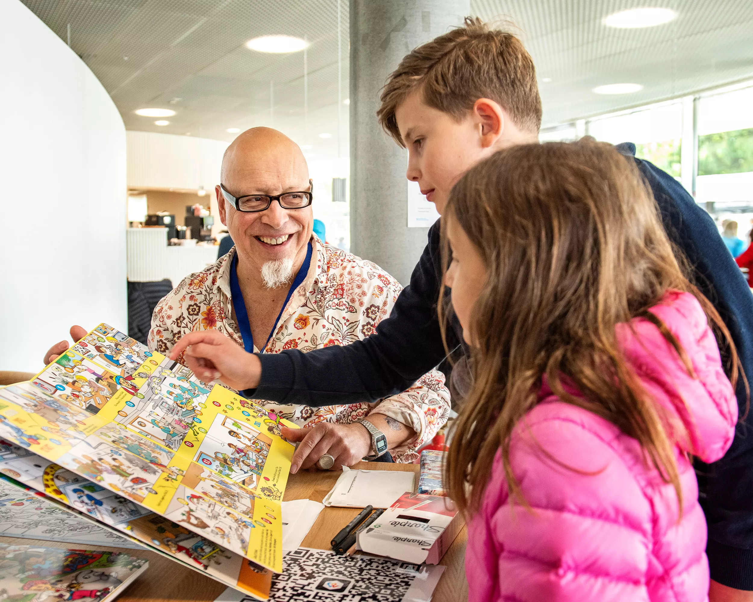 Ein Mann zeigt zwei Kindern ein Wimmelbuch.