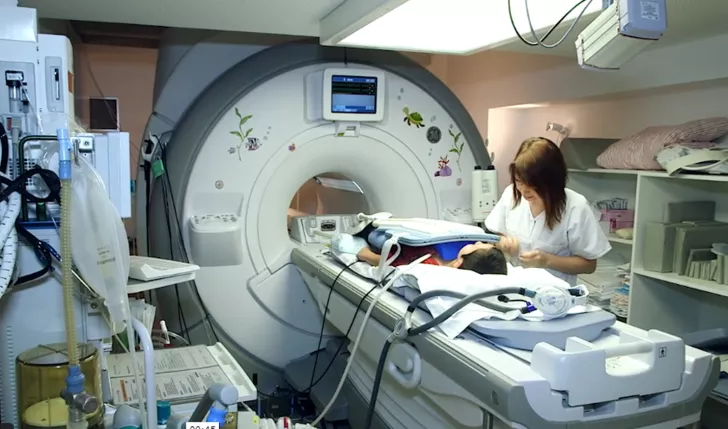 Ein Kind wird auf einer Trage in ein MRI gefahren, eine Fachperson steht daneben.
